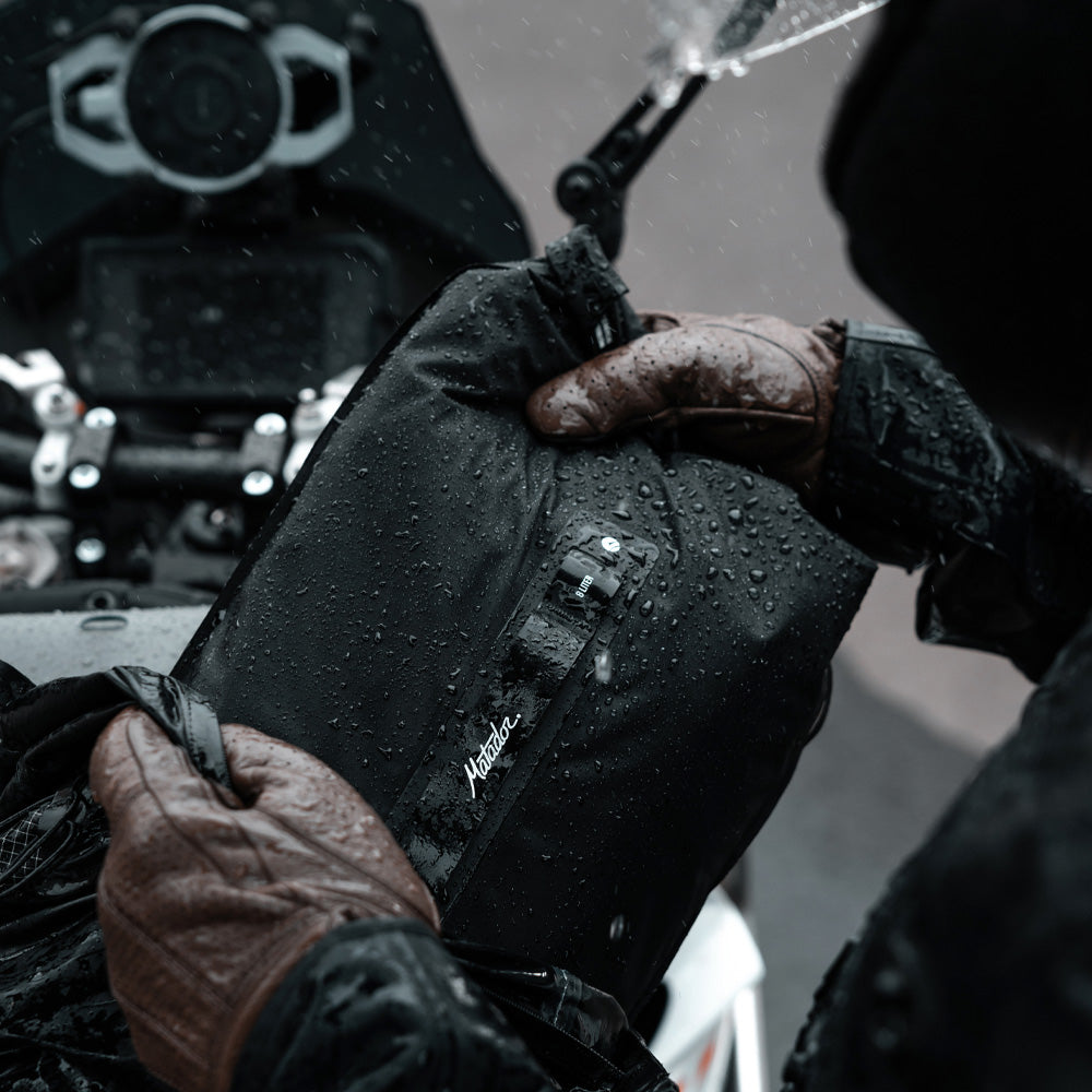 Close up view of motorcyclist placing rain covered dry bag into backpack